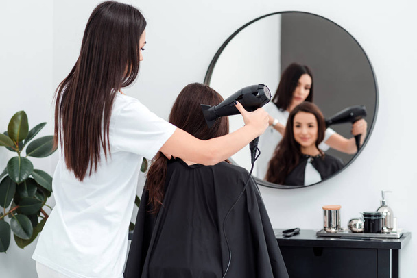Peluquería enfocada trabaja secando el cabello de un hermoso cliente
 - Foto, Imagen
