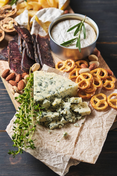 Delicious snacks. Several varieties of cheese, pretzels, nuts and sausage on an old wooden table. Food for a romantic dinner. - Photo, Image