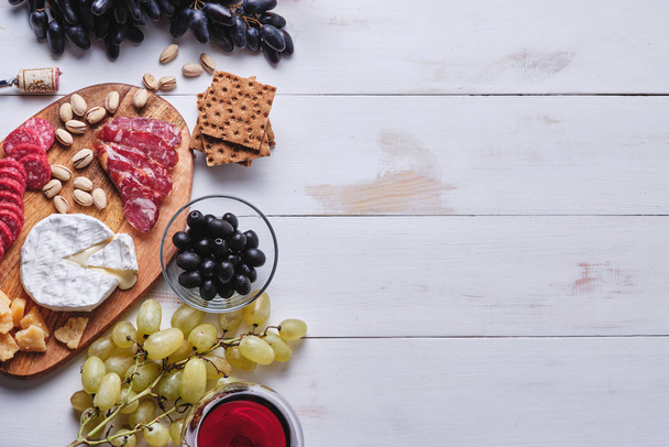 Νόστιμα προϊόντα για ένα ρομαντικό δείπνο. Τυρί και λουκάνικα, ξηροί καρποί, φρούτα, ελιές, ψωμί, σταφύλια, κρασί και μέλι σε ένα παλιό λευκό ξύλινο τραπέζι. Άποψη από ψηλά. - Φωτογραφία, εικόνα