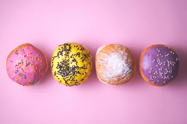 Four donuts with colored glaze on a pink paper background. - Foto, afbeelding