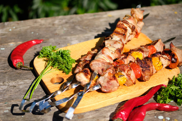 Freshly cooked barbecue and vegetables on a wooden table. Summer lunch in nature. Tasty meat dish cooked on the fire. - Photo, Image