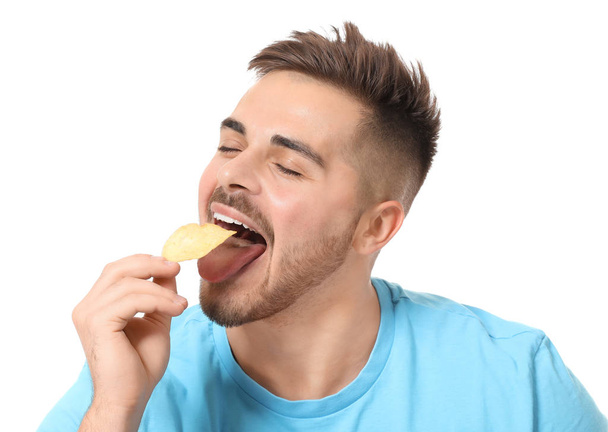 schöner junger Mann isst leckere Kartoffelchips auf weißem Hintergrund - Foto, Bild