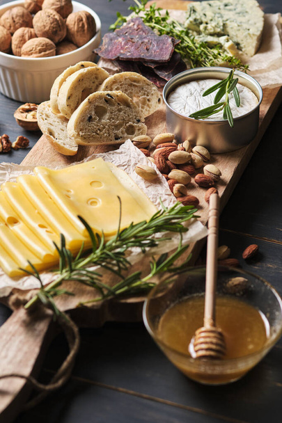Tasting different types of cheese, honey, nuts and herbs. Several varieties of cheese on a wooden board. Delicatessen for a romantic dinner. - Photo, Image