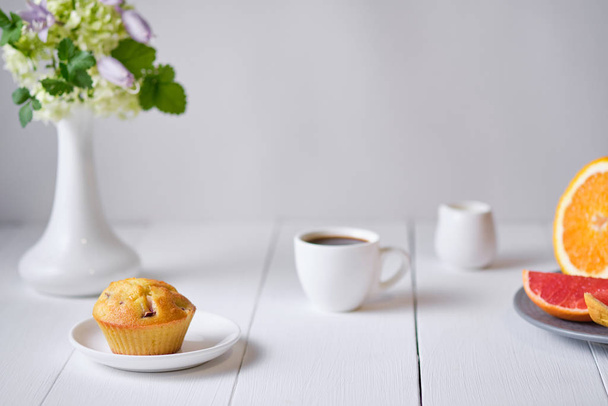 Καφές και κέικ φρούτων με φρέσκο ροδάκινο για πρωινό. Πρωινό τραπέζι με επιδόρπιο, εσπρέσο, φρούτα και λουλούδια σε βάζο σε λευκό ξύλινο τραπέζι. - Φωτογραφία, εικόνα