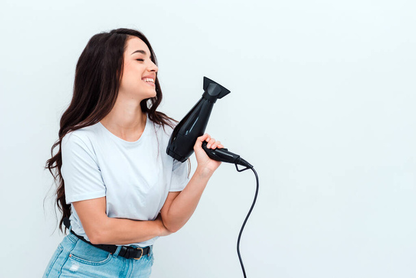 Beautiful girl with long dark hair holds a hairdryer on a white background - 写真・画像