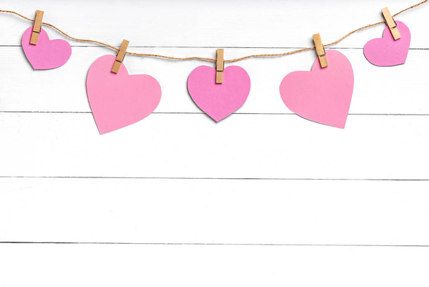 Clothespins with pink hearts hanging on rope behind white wooden surface. - Photo, Image