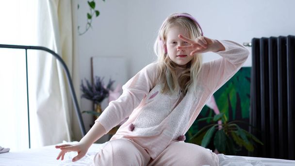 nowoczesne życie pokolenia Z. nastolatka w piżamie i słuchawki w pokoju na łóżku słucha muzyki ze smartfona. - Zdjęcie, obraz