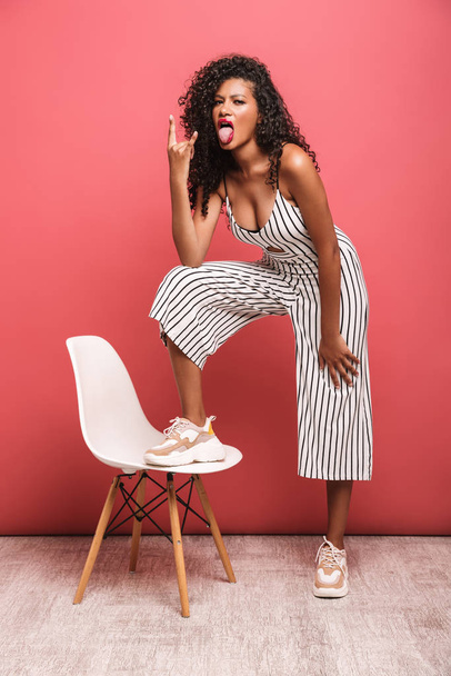 Image of african american woman showing horn fingers by chair - Foto, imagen