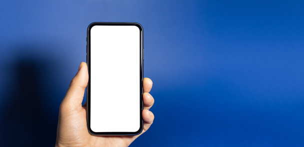 Close-up van de mannelijke hand holding smartphone met witte mockup geïsoleerd op fantoomblauwe achtergrond. - Foto, afbeelding