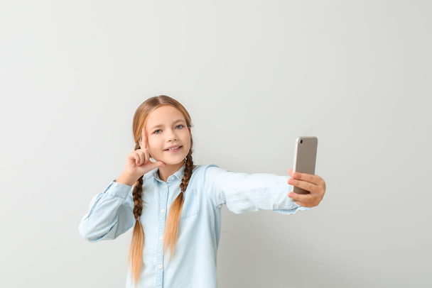 Linda niña tomando selfie sobre fondo claro
 - Foto, Imagen