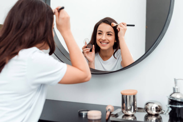 Beautiful, smiling, young woman doing her makeup - Photo, Image
