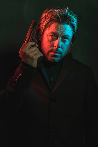 Mann hält Pistole neben Kopf rot und blau beleuchtet  - Foto, Bild