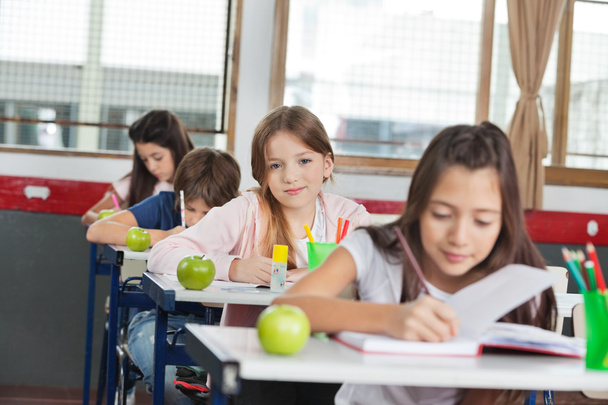 Schoolgirl Sitting At Desk With Classmates In A Row - Фото, зображення