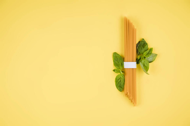 Spaghetti, basil on a yellow background. Top view. Copy space for text. - Zdjęcie, obraz