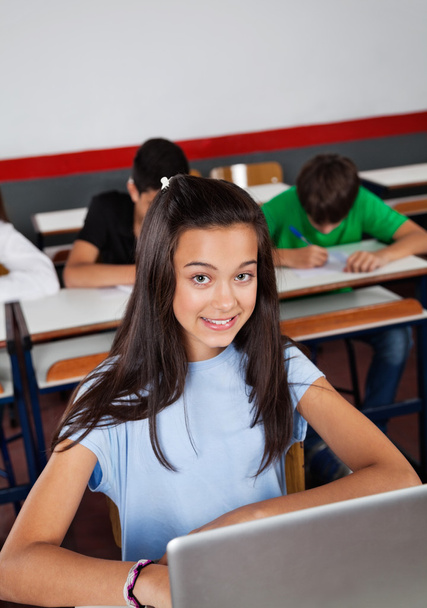 Onnellinen teini koulutyttö istuu kannettava tietokone pöydällä
 - Valokuva, kuva