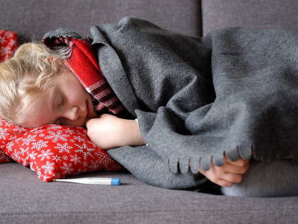 chica caucásica fría en casa. retrato de un niño enfermo en una bufanda y a cuadros en el sofá en el apartamento
 - Foto, Imagen