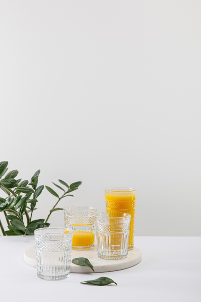 glasses of delicious yellow smoothie on white surface near green plant isolated on grey - Φωτογραφία, εικόνα