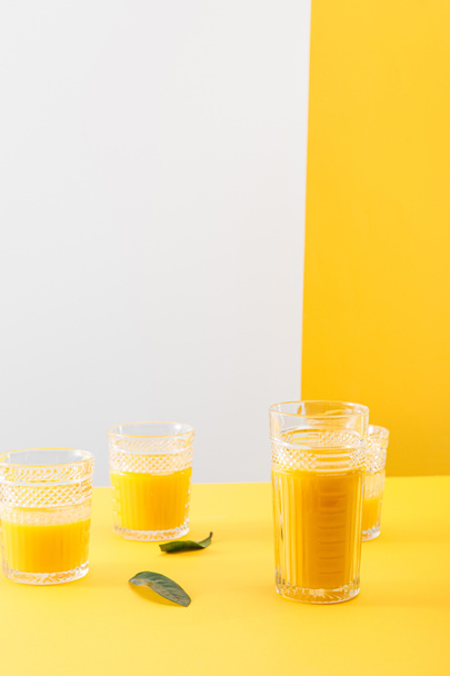 glasses of fresh delicious yellow smoothie near green leaves - Foto, afbeelding