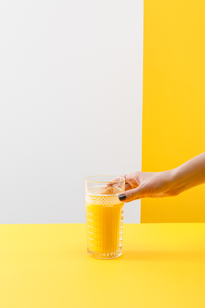 cropped view of woman holding glass of fresh delicious yellow smoothie on grey and yellow background - Photo, Image