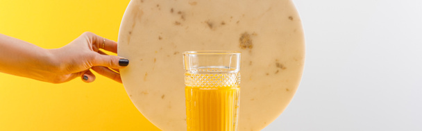 cropped view of woman holding marble circle near glass of fresh delicious yellow smoothie on grey and yellow background, panoramic shot - Fotografie, Obrázek