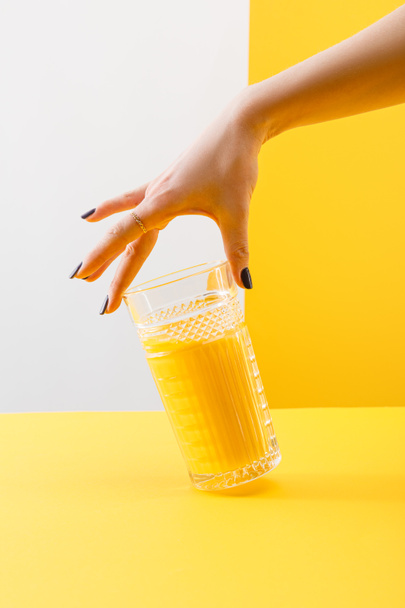 bijgesneden uitzicht op vrouw met een glas verse heerlijke gele smoothie op grijze en gele achtergrond - Foto, afbeelding