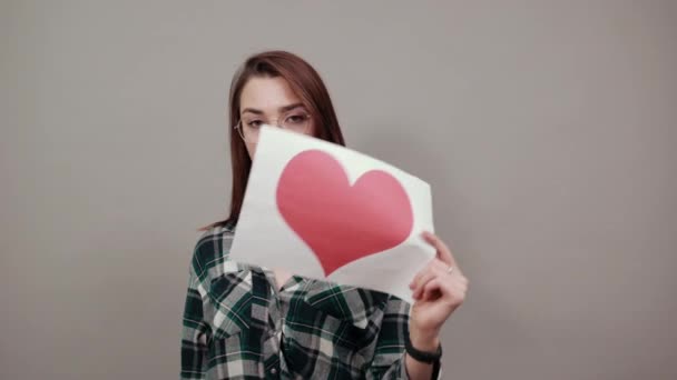 unhappy woman with glasses holds piece of paper with red heart in hand - Video, Çekim