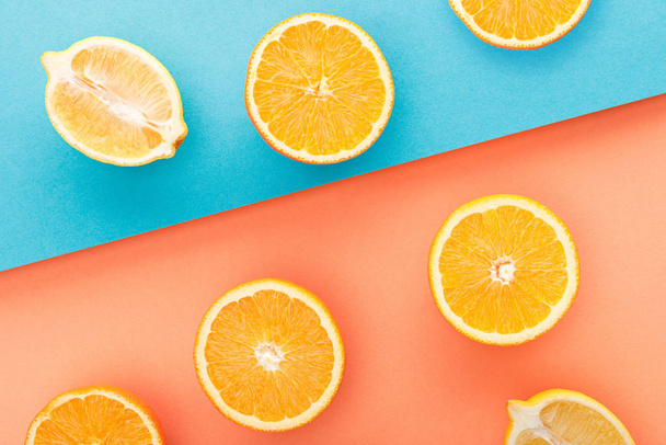 Top view of cut oranges and lemon halves on blue and orange background - Foto, Imagem