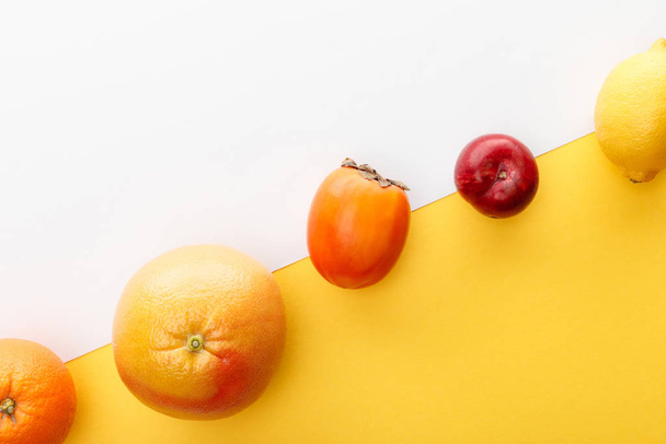 Vista superior de naranja, pomelo, limón, caqui y manzana sobre fondo amarillo y blanco
 - Foto, Imagen