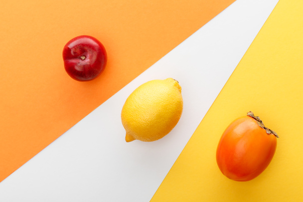 Top view of lemon, persimmon and apple on yellow, orange and white background - 写真・画像