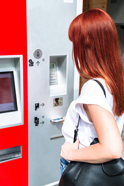 Young redhead woman inserts banknote into terminal - Photo, image