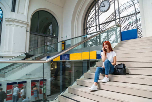 Girl with phone sitting on steps of waiting hall - Zdjęcie, obraz