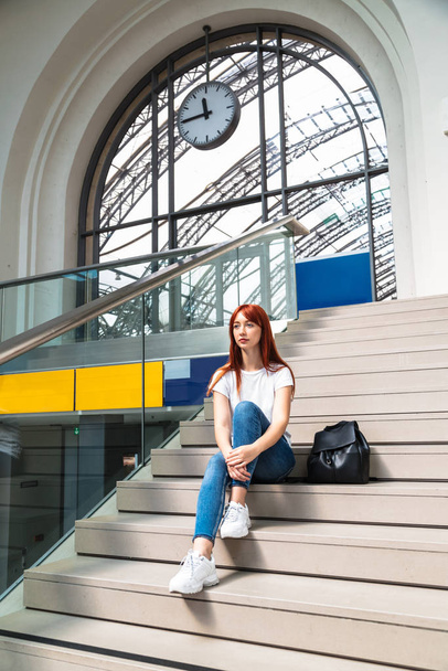 Girl with pensive look sits on stairs of station - Photo, Image