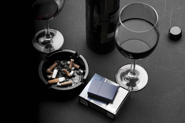 Cigarette in an ashtray, glass of wine and bottle of wine  - Photo, Image