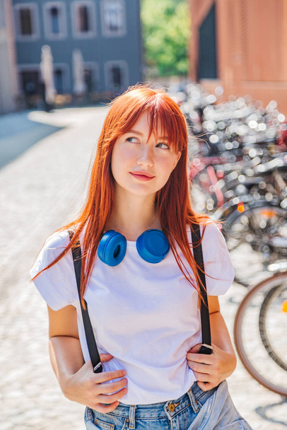 Cute redhead girl having fun on street near bikes - Фото, зображення