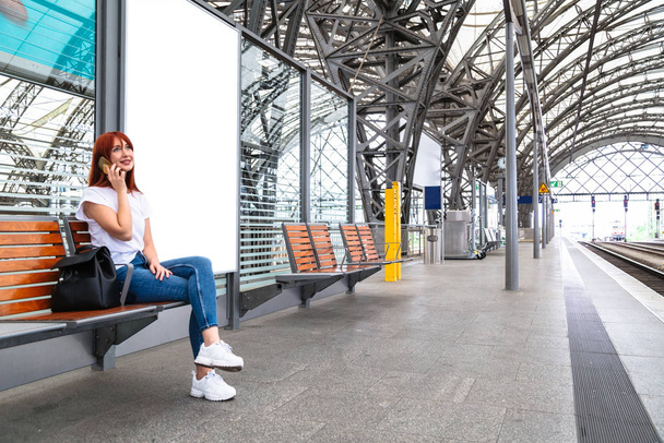 Traveler girl sitting on wooden bench on station - Foto, afbeelding