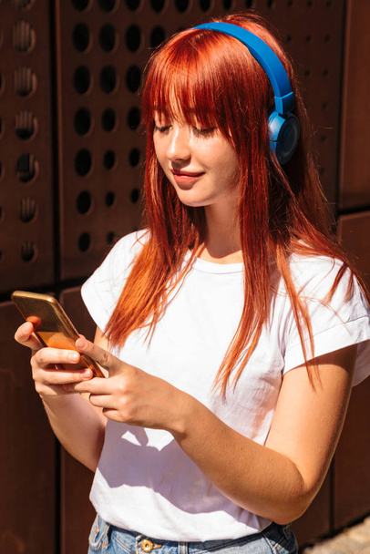 Redhead woman listening wireless music with headphones - 写真・画像