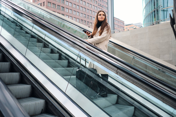 Young beautiful businesswoman with suitcase on escalator outdoor - Foto, Bild