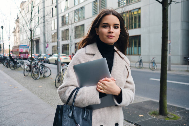 Young stylish businesswoman with laptop confidently walking through city street - Foto, imagen
