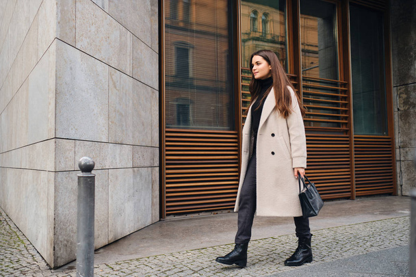 Красива стильна брюнетка дівчина в пальто щасливо ходить по міській вулиці
 - Фото, зображення
