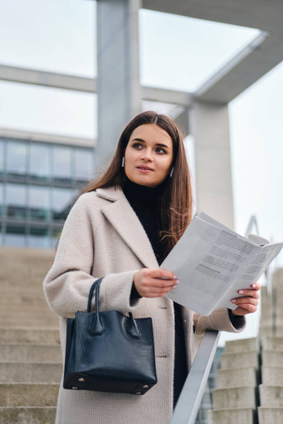 Attractive casual businesswoman with handbag reading newspaper outdoor - Fotó, kép