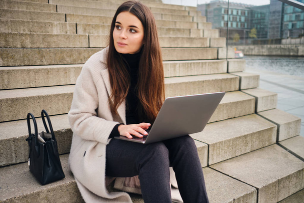Jonge stijlvolle zakenvrouw werkt op laptop zitten op de trap buiten - Foto, afbeelding