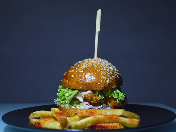 tasty burger, juicy fresh bun with sesame seeds inside vegetables, cutlet and sauce, near french fries - Foto, afbeelding