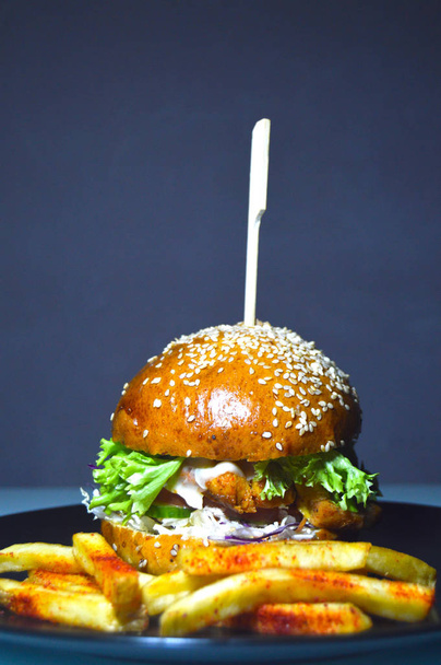 tasty burger, juicy fresh bun with sesame seeds inside vegetables, cutlet and sauce, near french fries - Photo, image