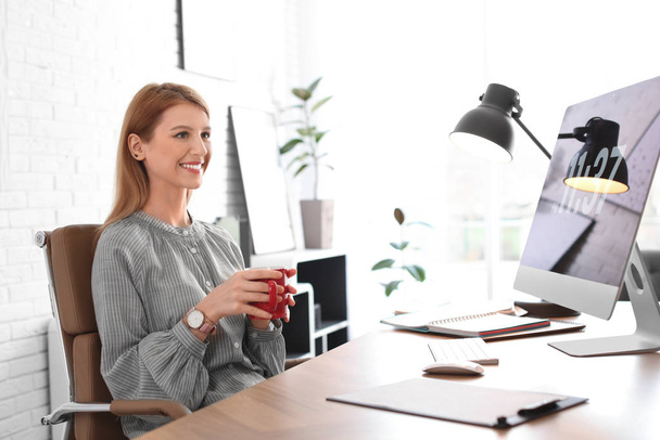 Young woman with cup of drink relaxing at table in office during - Foto, Bild