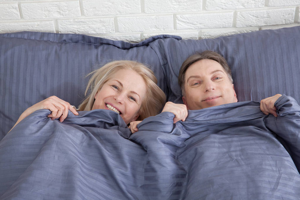 Happy couple is lying in bed together. Enjoying the company of each other. - Valokuva, kuva