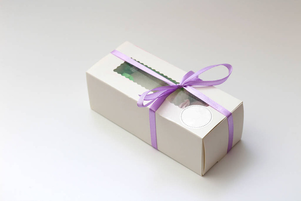 Bílá kartonová krabička s průhledným víčkem a fialovou stuhou izolovanou na bílém pozadí. Nádherný dárek na Valentýna, narozeniny. - Fotografie, Obrázek