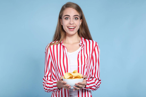 Young beautiful girl with potato chips in bowl on blue backgroun - Foto, Imagem