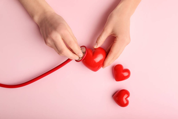Female hands with red hearts and stethoscope on color background. Cardiology concept - Photo, Image