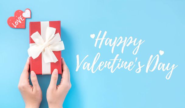 Valentine's Day gift card with greeting word design concept, woman sending gift on vibrant blue background, top view, overhead. - Photo, Image