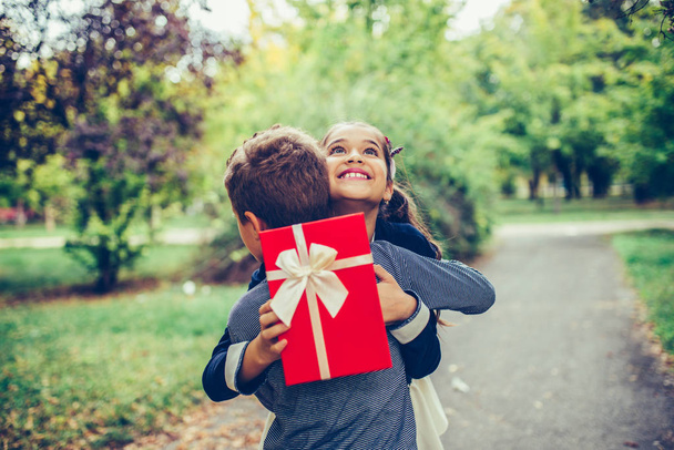 glücklicher kleiner Junge schenkt lächelndem Mädchen eine Geschenkschachtel und macht ein s - Foto, Bild